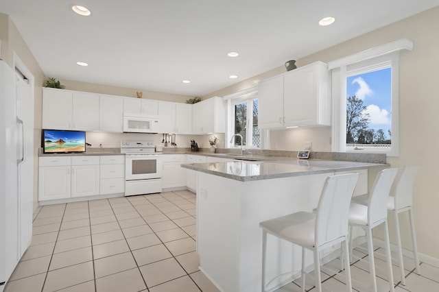 kitchen with white cabinets, a peninsula, recessed lighting, a kitchen bar, and white appliances