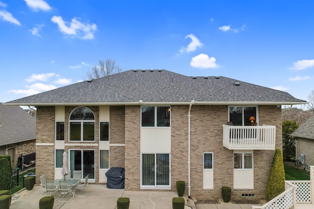 back of house featuring brick siding, a patio area, a balcony, and a shingled roof