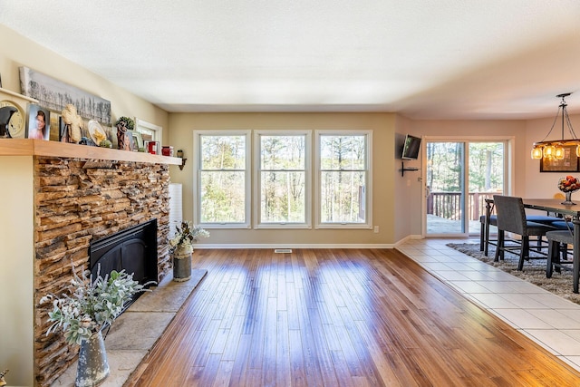 living area with hardwood / wood-style floors, a stone fireplace, visible vents, baseboards, and a notable chandelier