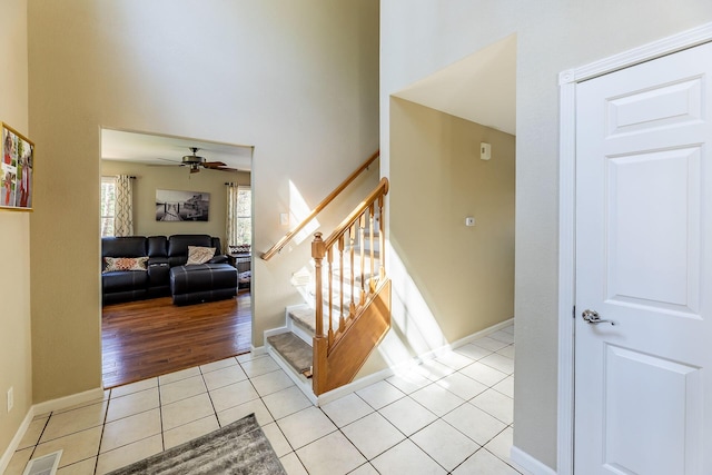 staircase featuring ceiling fan, a towering ceiling, baseboards, tile patterned flooring, and visible vents