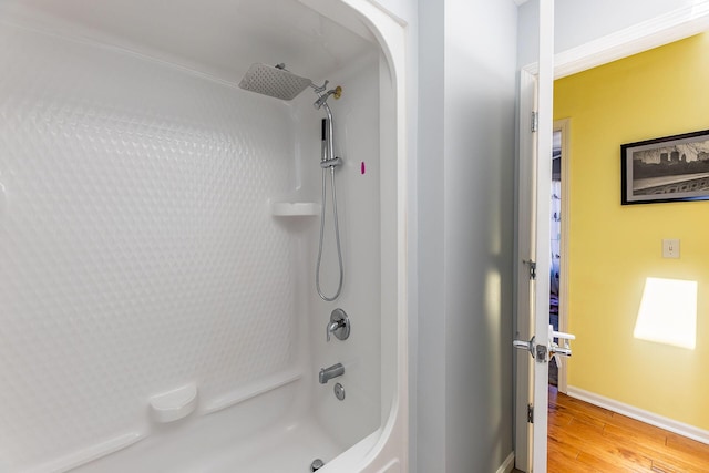 bathroom featuring baseboards, wood finished floors, and shower / tub combination