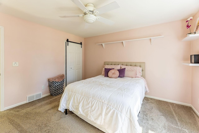 bedroom with a barn door, visible vents, a ceiling fan, carpet floors, and baseboards