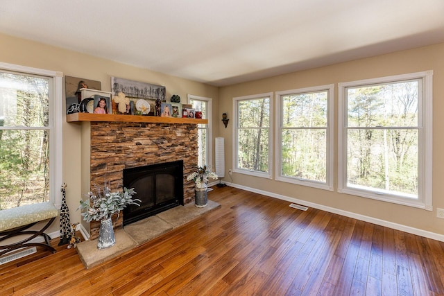 living room featuring wood-type flooring, visible vents, baseboards, and a fireplace