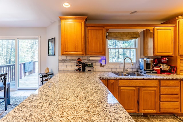 kitchen featuring backsplash, brown cabinetry, light stone countertops, and a sink