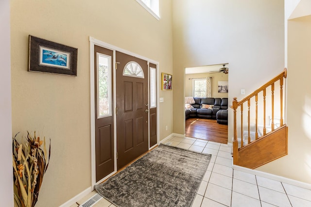 foyer featuring a towering ceiling, light tile patterned floors, baseboards, stairs, and ceiling fan