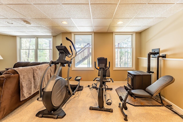 workout room featuring a paneled ceiling, baseboards, carpet floors, and a wood stove