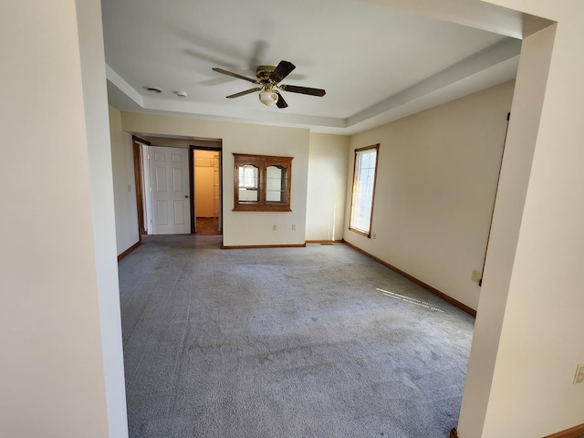 spare room with a raised ceiling, carpet floors, baseboards, and ceiling fan
