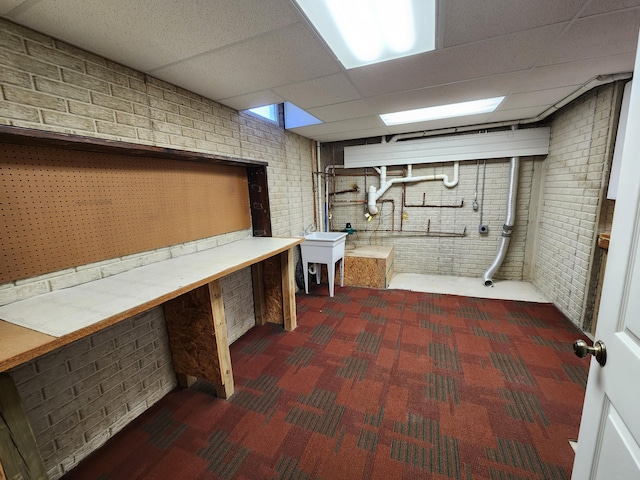 finished below grade area with a paneled ceiling, carpet flooring, and brick wall