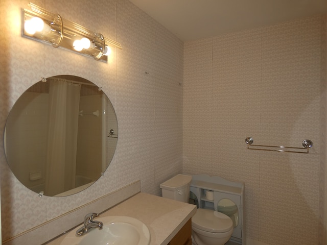 bathroom with toilet, vanity, and wallpapered walls