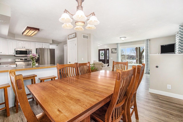 dining area with baseboards, a chandelier, wood finished floors, and visible vents