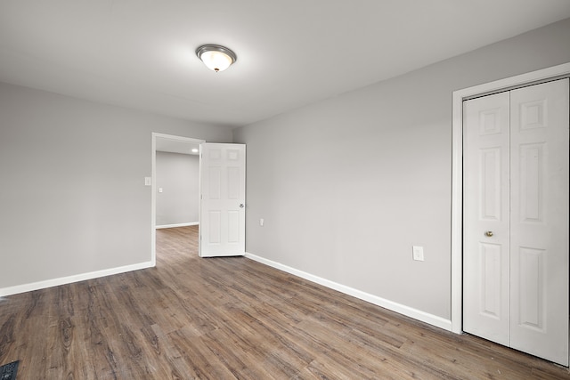 unfurnished bedroom with baseboards, wood finished floors, visible vents, and a closet
