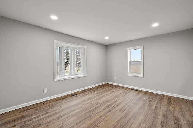 unfurnished room featuring baseboards, wood finished floors, visible vents, and a wealth of natural light