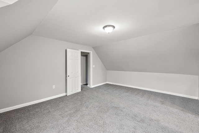 additional living space with vaulted ceiling, dark colored carpet, and baseboards