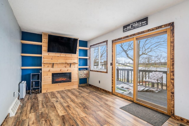 unfurnished living room featuring a glass covered fireplace, wood finished floors, visible vents, and baseboards