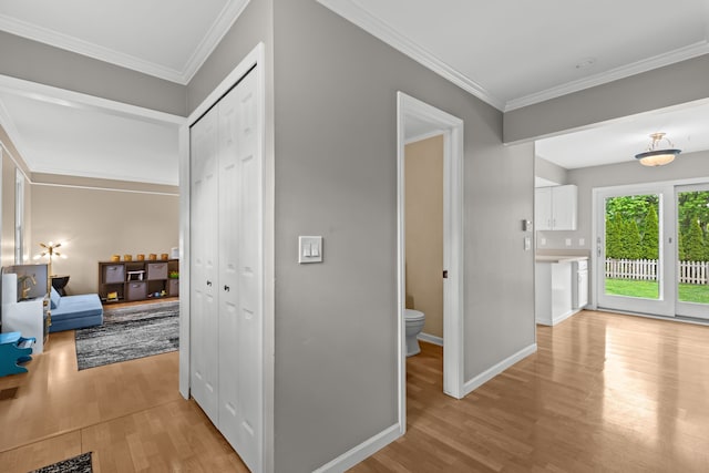 corridor with light wood finished floors, crown molding, and baseboards