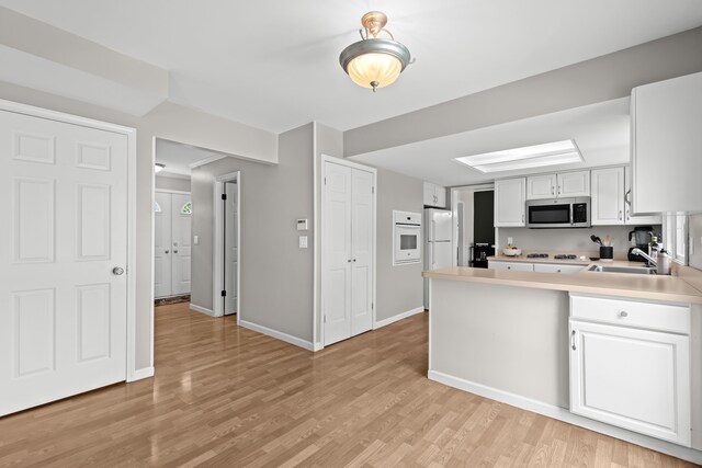 kitchen with white appliances, white cabinetry, a peninsula, light countertops, and light wood-type flooring