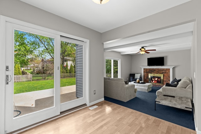 living area featuring wood finished floors, a brick fireplace, visible vents, baseboards, and ceiling fan
