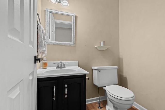 half bathroom featuring toilet, baseboards, wood finished floors, and vanity