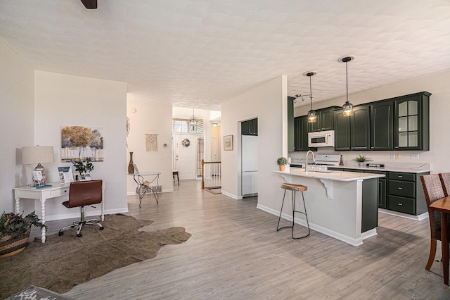 kitchen with a sink, white appliances, light countertops, light wood-style flooring, and a kitchen bar