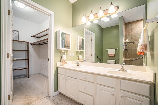 bathroom with a tile shower, toilet, a sink, and double vanity