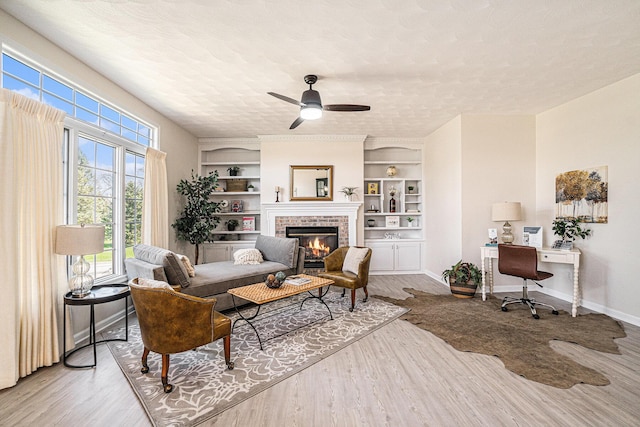 living room featuring wood finished floors, a fireplace, a textured ceiling, built in shelves, and ceiling fan