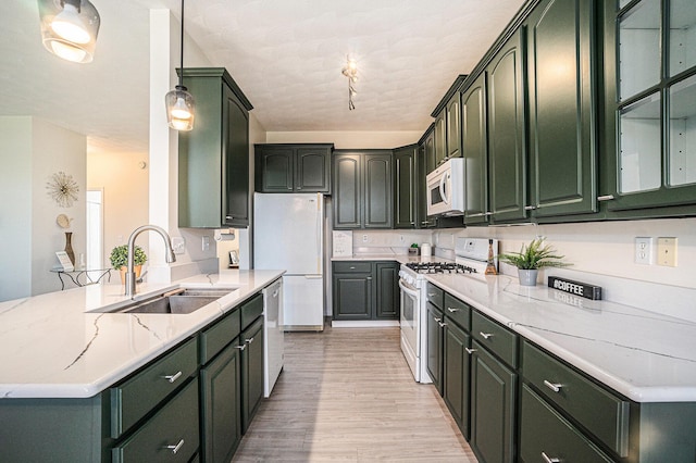 kitchen with light wood finished floors, green cabinetry, a sink, and white appliances
