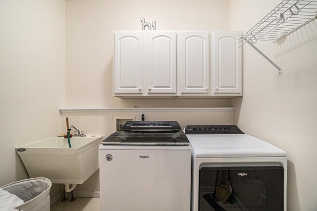 clothes washing area featuring washing machine and dryer, baseboards, a sink, and cabinet space