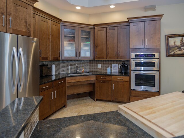 kitchen with a sink, recessed lighting, backsplash, glass insert cabinets, and appliances with stainless steel finishes