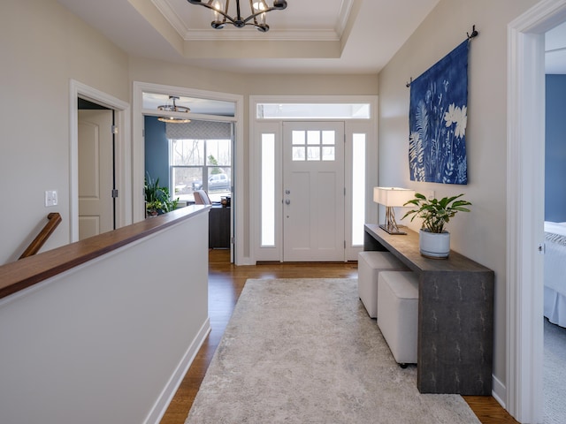 foyer featuring a raised ceiling, wood finished floors, crown molding, and a notable chandelier