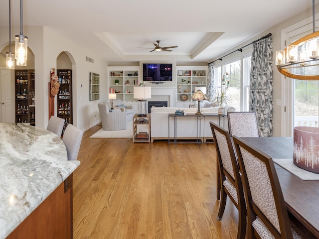dining room featuring a tray ceiling, light wood-style floors, visible vents, and a ceiling fan