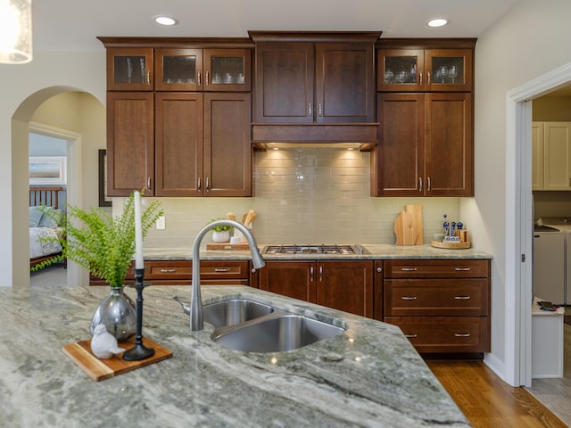 kitchen featuring arched walkways, a sink, washing machine and dryer, wood finished floors, and light stone counters