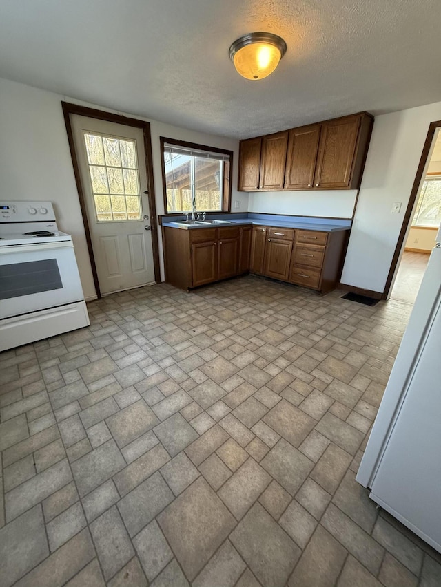 kitchen with white electric stove, a sink, baseboards, brown cabinets, and brick patterned floor