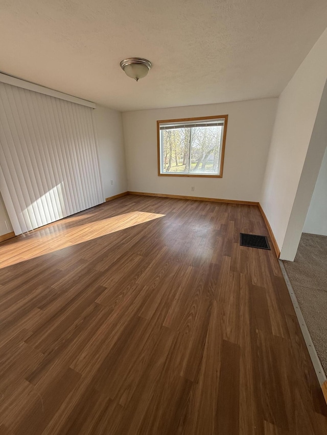 unfurnished room with baseboards, visible vents, and dark wood-style floors
