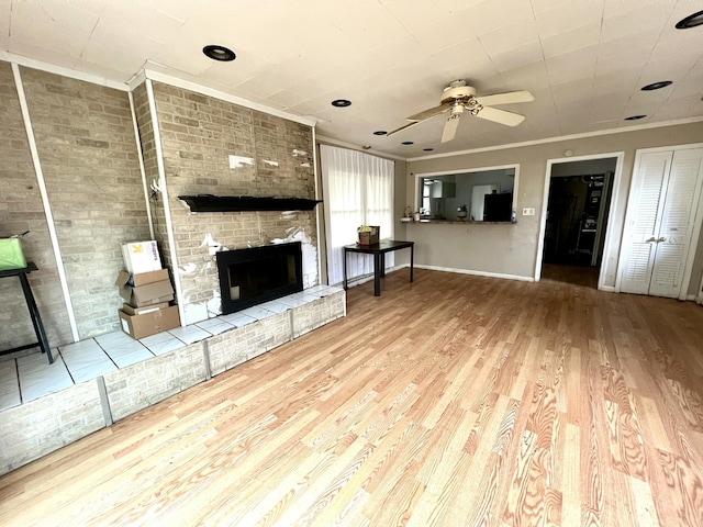 unfurnished living room featuring baseboards, a brick fireplace, wood finished floors, ceiling fan, and ornamental molding