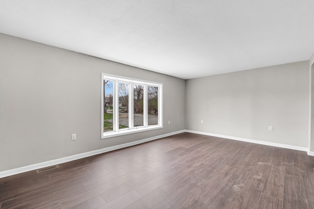unfurnished room with dark wood-type flooring, visible vents, and baseboards