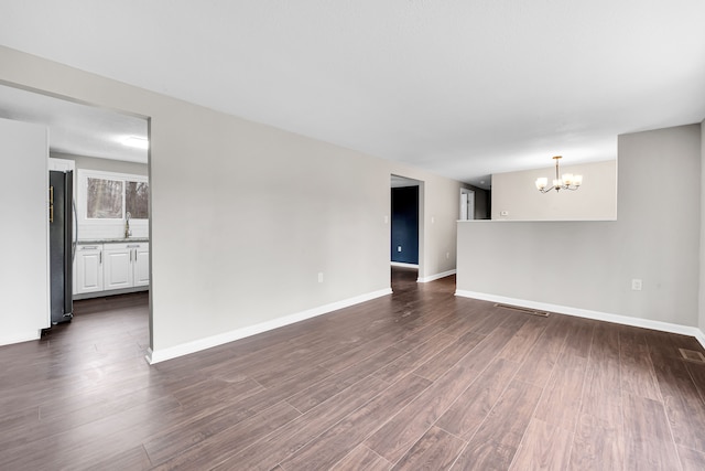 unfurnished living room with dark wood finished floors, baseboards, a sink, and an inviting chandelier