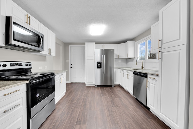 kitchen with dark wood finished floors, stainless steel appliances, a sink, a textured ceiling, and white cabinetry