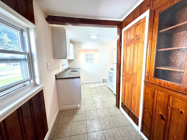 kitchen featuring a sink, gas range gas stove, baseboards, white cabinetry, and light tile patterned floors