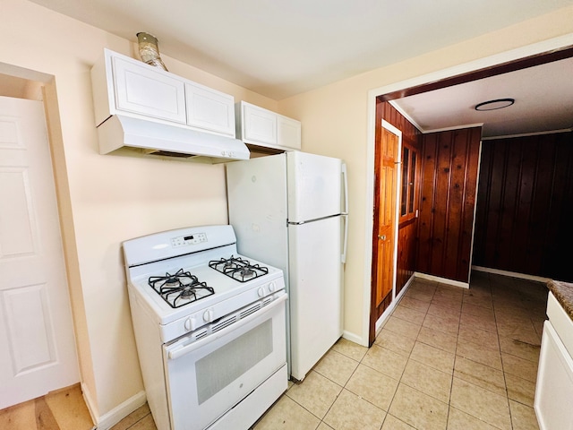 kitchen featuring wood walls, under cabinet range hood, light tile patterned floors, white appliances, and white cabinetry