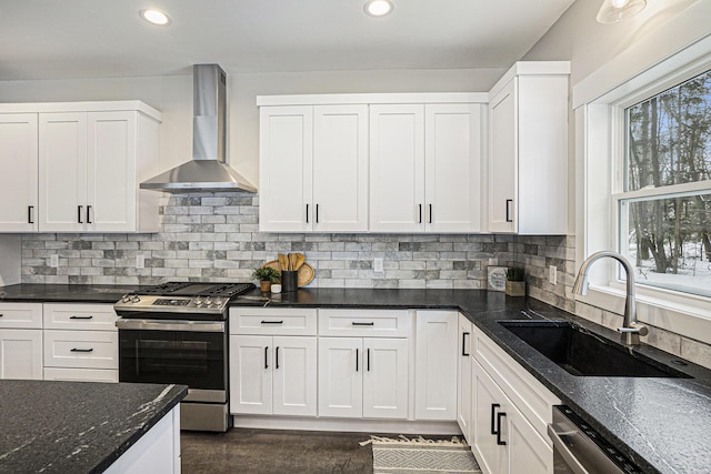 kitchen featuring white cabinets, recessed lighting, stainless steel appliances, wall chimney range hood, and a sink