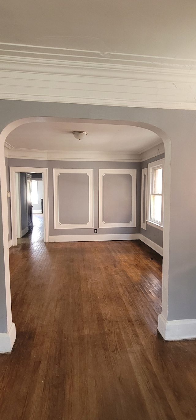 corridor featuring baseboards, arched walkways, dark wood-type flooring, and ornamental molding