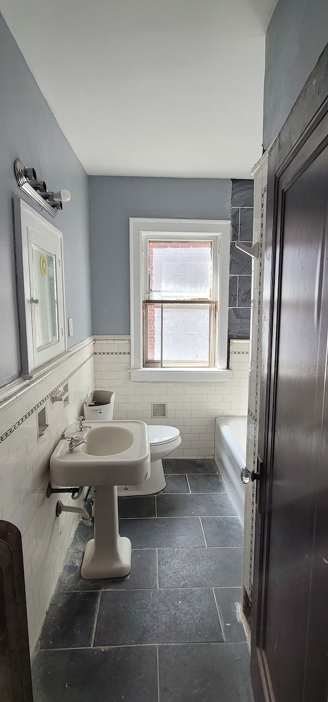 full bathroom with tile walls, a bathing tub, toilet, and wainscoting
