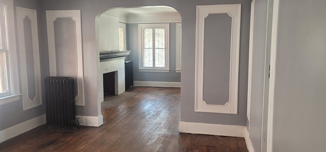 unfurnished living room with dark wood-type flooring, radiator heating unit, arched walkways, and baseboards