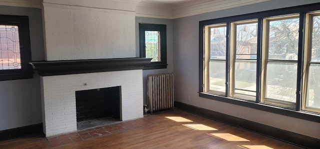 unfurnished living room featuring radiator heating unit, wood finished floors, a brick fireplace, and crown molding