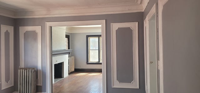 hallway with radiator heating unit, ornamental molding, and wood finished floors