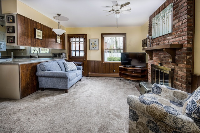 living room with a wainscoted wall, a fireplace, baseboard heating, ceiling fan, and light colored carpet