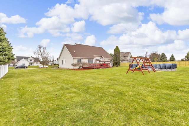 rear view of house with fence, a wooden deck, a yard, and a playground