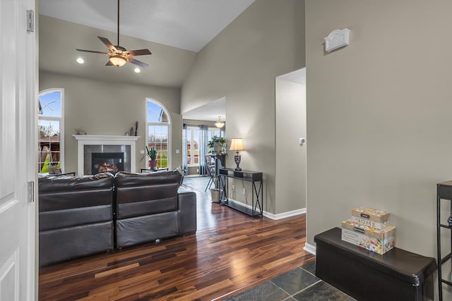 living area featuring high vaulted ceiling, a ceiling fan, wood finished floors, a tile fireplace, and baseboards