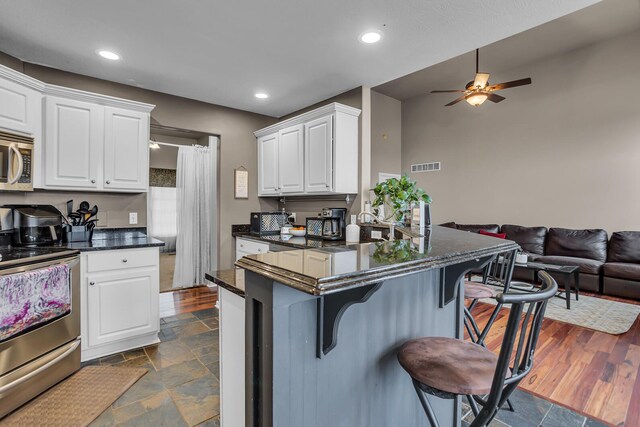 kitchen featuring stainless steel appliances, a kitchen breakfast bar, open floor plan, visible vents, and a ceiling fan