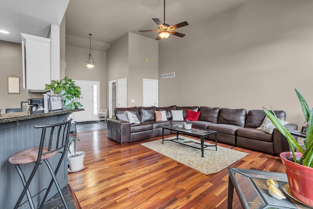living area featuring wood finished floors, visible vents, high vaulted ceiling, and ceiling fan